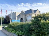 front of library. greenery in front, three flag poles with flags flying, blue skies