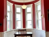 photograph of a rounded alcove with red walls, one desk and chair located in the center, big windows. 