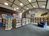 rows of children's book shelves, big comfy blue chair on rug with open seating in front of it