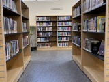 rows of books with a window above, white walls, wood and black shelves