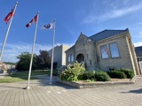 front of library. greenery in front, three flag poles with flags flying, blue skies
