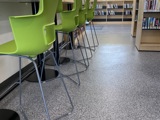 bar stool green seats lined up in front of a high table, shelves of books in the background